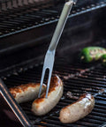 Grillgabel aus Stahl mit Würstchen auf dem Grill, perfekt zum Greifen und Anheben von Lebensmitteln, ohne sich zu verbrennen