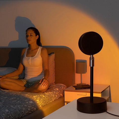 Frau bei Entspannung und Meditation mit einem Sonnenuntergangsprojektor im Schlafzimmer, romantische und entspannende Atmosphäre für das Wohlbefinden